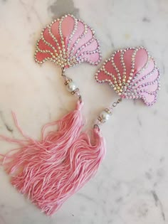 two pink tassels with pearls on them sitting on a marble counter top next to each other