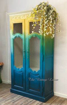 a tall blue cabinet with two doors and flowers in the top one is painted teal