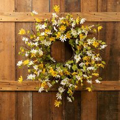 a wreath with yellow and white flowers hanging on a wooden wall