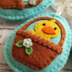 three felt easter baskets decorated with flowers and a rubber ducky in the center, on a white wooden surface