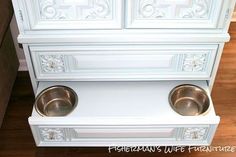 a white cabinet with two metal bowls on the front and bottom, sitting next to a wood floor