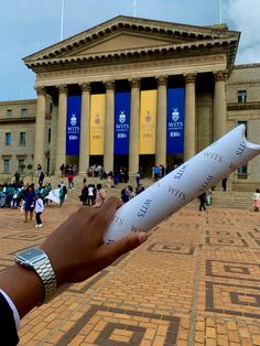 a person holding up a piece of paper in front of a building with columns and pillars