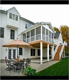 an outside patio with tables and umbrellas in front of a large white house on a cloudy day