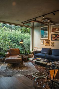 a living room filled with furniture next to a window covered in lots of plants and trees