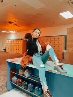 a woman sitting on top of a blue counter with lots of bowling balls in it