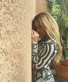 a woman leaning against a wall with her hand on her head