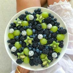 a white bowl filled with grapes, kiwis and blackberries on top of a woman's legs