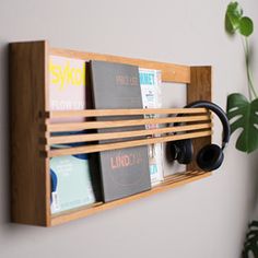 a wooden shelf holding books and headphones on top of a white wall next to a potted plant