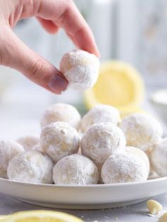 a person is picking up some food from a white plate with lemons on the side