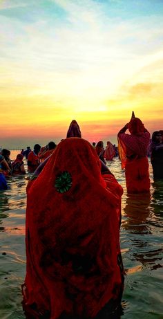 several people in the water at sunset with their backs to each other, wearing red cloths