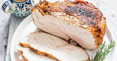 sliced pork on a white plate next to a cup of coffee and saucer with sprig of rosemary