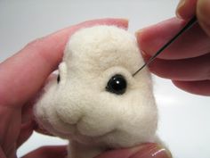 someone is needleing the end of a small stuffed animal with black eyeballs on it