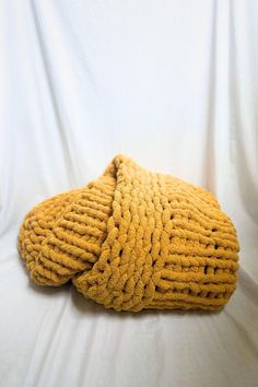 a yellow knitted object laying on top of a white cloth covered bed spreader