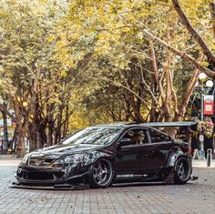 a black car parked on the side of a brick road next to trees and street lights