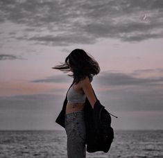 a woman standing on the beach with her hair blowing in the wind and looking at the ocean