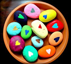 colorful rocks in a bowl with hearts painted on them, sitting on a wooden table