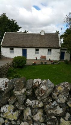 a white house with a thatched roof next to a stone wall and green grass