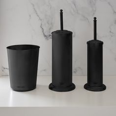 three black candlesticks and one candle holder on a marble countertop with white marble behind them