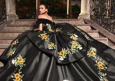 a woman wearing a black dress with sunflowers on it sitting on some steps