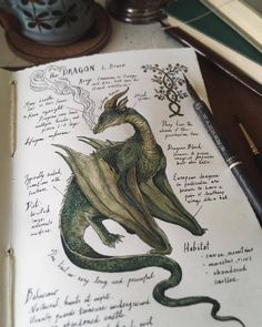 a drawing of a green dragon sitting on top of a book next to a pen