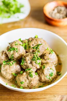 a white bowl filled with meatballs covered in gravy and garnished with parsley