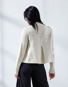 a woman standing in front of a white wall wearing black pants and a cream sweater