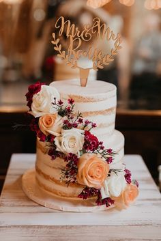 a wedding cake decorated with flowers and a mr and mrs topper on a table