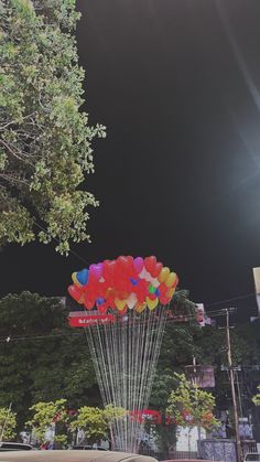 a bunch of balloons are floating in the air near a tree and some cars parked on the street