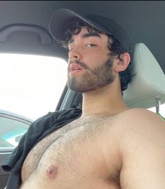 a shirtless man sitting in the back seat of a car wearing a baseball cap