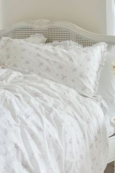 a bed with white sheets and pink flowers on the comforter, next to a window