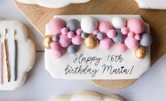 a birthday cake decorated with pink, grey and white balloons on a cutting board next to cookies