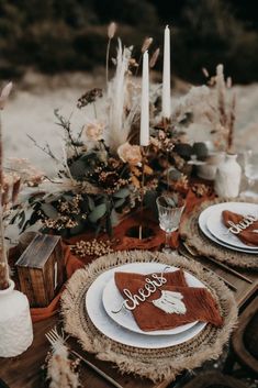 the table is set with white plates and brown napkins, silverware and candles