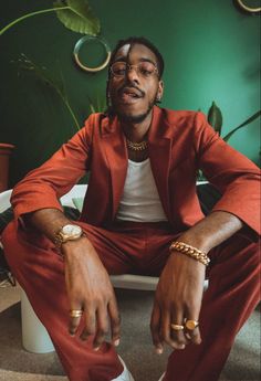 a man in a red suit sitting on a white chair with his hands crossed and wearing gold rings