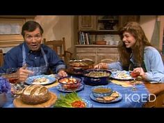 two people sitting at a table with plates of food in front of them and one person pointing to the camera