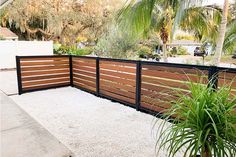 a wooden fence in front of a house with palm trees and gravel on the ground