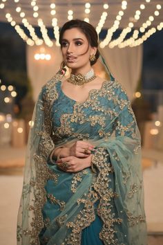 a woman in a blue sari and gold jewelry poses for the camera with her hand on her hip