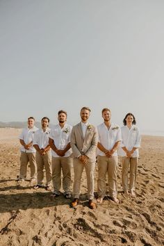 a group of men standing next to each other on top of a sandy beach near the ocean