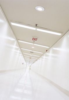 an exit sign is shown on the ceiling in this long hallway with white walls and floors