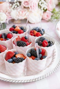 small cups filled with berries and strawberries on a plate next to pink flower arrangements