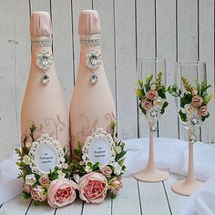 three champagne bottles with flowers on them sitting next to two wine glasses and one vase