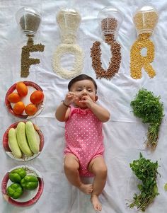 a baby is laying down in front of some vegetables and fruits on a table with the word food spelled out