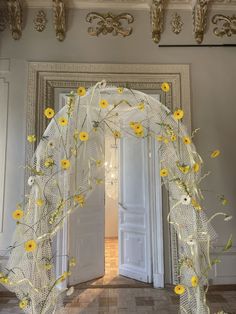 a white arch with yellow flowers on it in front of an open door and chandelier