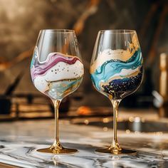 two wine glasses sitting on top of a counter next to each other with different designs