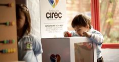 a young child playing with a box in front of a sign that says cirec