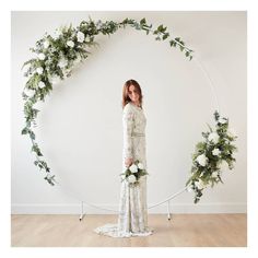 a woman standing in front of a white circle with flowers and greenery on it