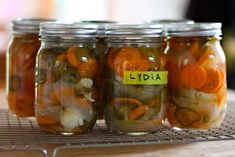 four jars filled with pickles and onions on a shelf next to a wire rack