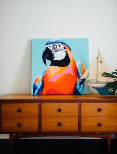 a painting of a parrot sitting on top of a dresser next to a sailboat