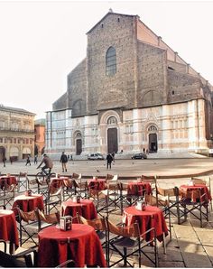 tables and chairs are set up in front of an old church with red cloths on them