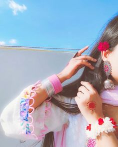 a woman with long black hair wearing pink and white clothing holding onto her earring