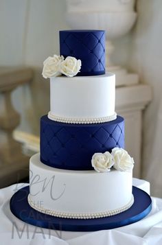 a three tiered wedding cake with white flowers on top and blue ribbon around the bottom